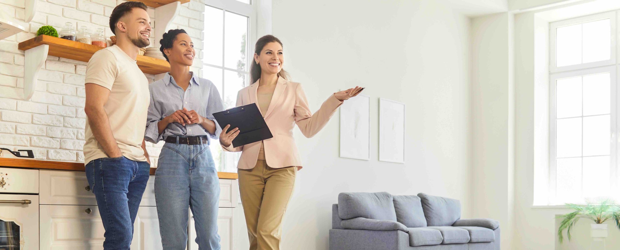 Real estate agent showing bright apartment interior to smiling young couple A couple being shown around a house - The Process of Buying a House